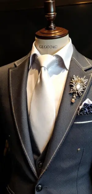 Grey suit with a white tie, pearl brooch, and pocket square.