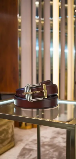 Dark brown leather belt with a silver buckle in a luxury showroom.