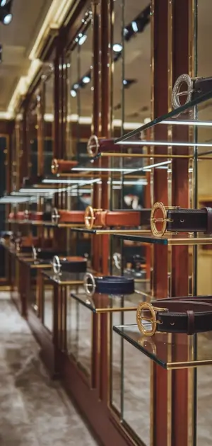 Glass shelves showcasing a variety of belts with circular and rectangular buckles.