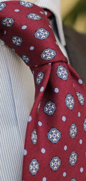 A red neck tie for men with intricate blue and white patterns, paired with a striped shirt.