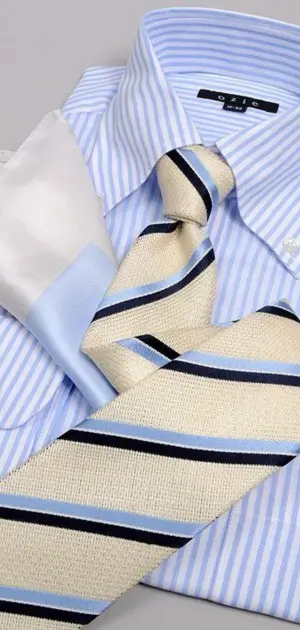Close-up of a striped tie, blue pocket square, and light blue striped shirt.