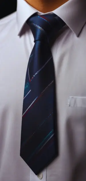 A man wearing a solid navy silk tie paired with a crisp white shirt and charcoal suit.