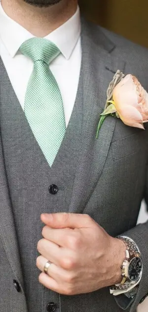 A pastel green tie and grey suit combination styled with a boutonniere.