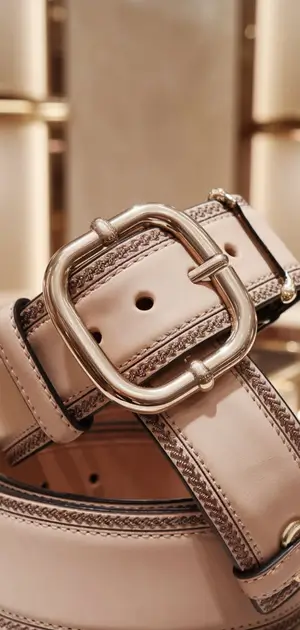 Beige leather belt with a round buckle on a glass display in a stylish showroom
