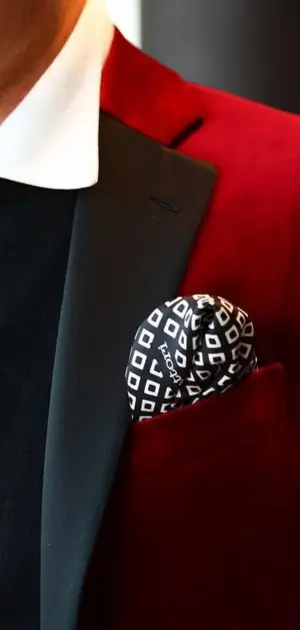 Close-up of a red velvet blazer featuring black lapels and a bold pocket square with geometric patterns.