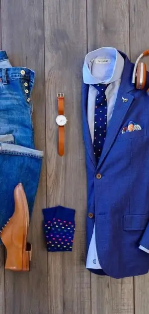 Flat lay of men’s athletic suit accessories: blue blazer, tie, jeans, leather shoes, and watch.