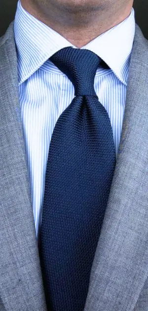 Men's navy blue textured tie paired with a striped shirt and gray blazer, ideal for professional attire.