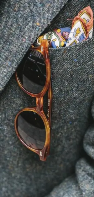 Close-up of a tweed suit featuring tortoiseshell sunglasses and a pocket square.