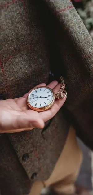 Man holding a gold pocket watch, complementing a vintage tweed suit style.