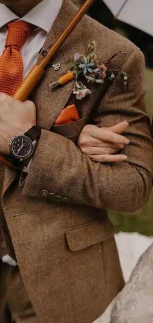 How to wear a suit to a wedding Groom wearing a tweed suit accessorized with orange tie, boutonniere, and watch.