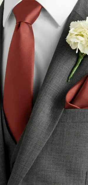 Red ties for men near me A polished red tie styled with a gray suit and a white flower boutonniere.