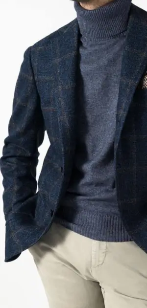 Men’s navy checkered sports blazer styled with a grey turtleneck and beige trousers.