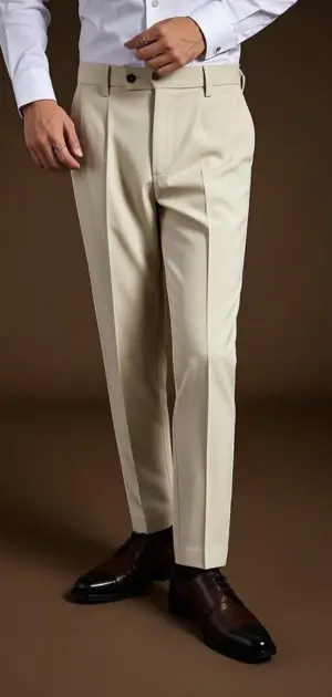 A man dressed in beige tailored pants, a white shirt, and brown shoes.