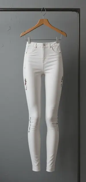 White embroidered skinny leggings hanging neatly on a hanger.